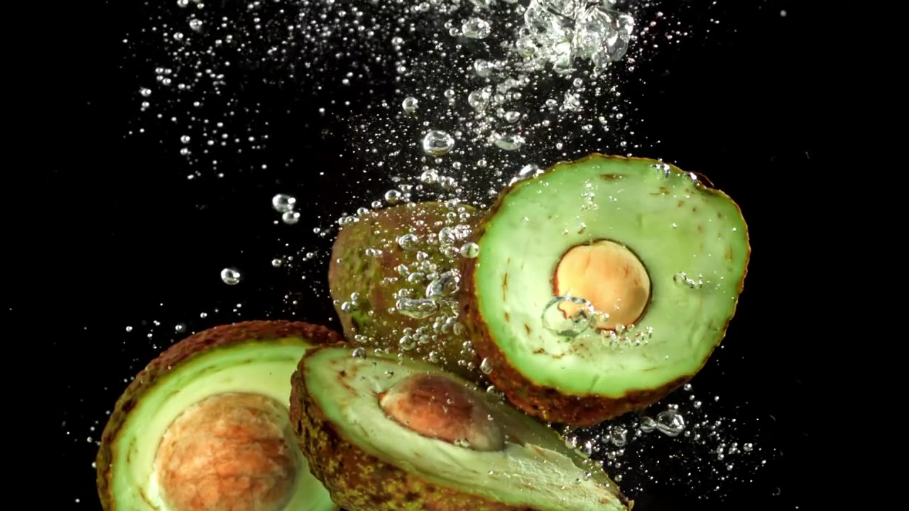 Metà di avocado fresco che si tuffano nell'acqua al rallentatore