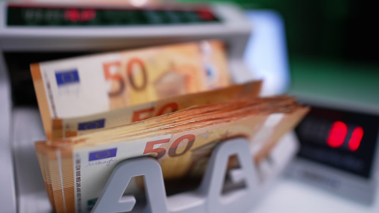 Orange bills of fifty euro value and green ones of hundreds fall on the holder of cash counting machine. Close up. Banking equipment.