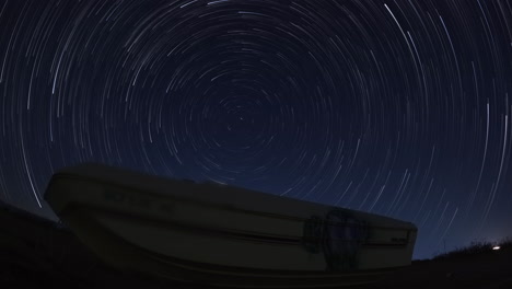 een oude verlaten boot gedumpt langs een weg in de mojave-woestijn op de voorgrond van een polaris star trails time-lapse