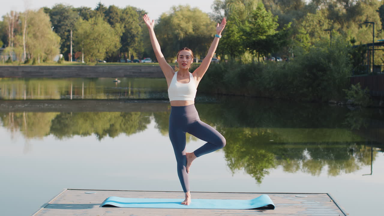 atractiva mujer joven entrenadora deportiva en ropa deportiva de pie en postura de árbol de yoga cerca del estanque en el parque