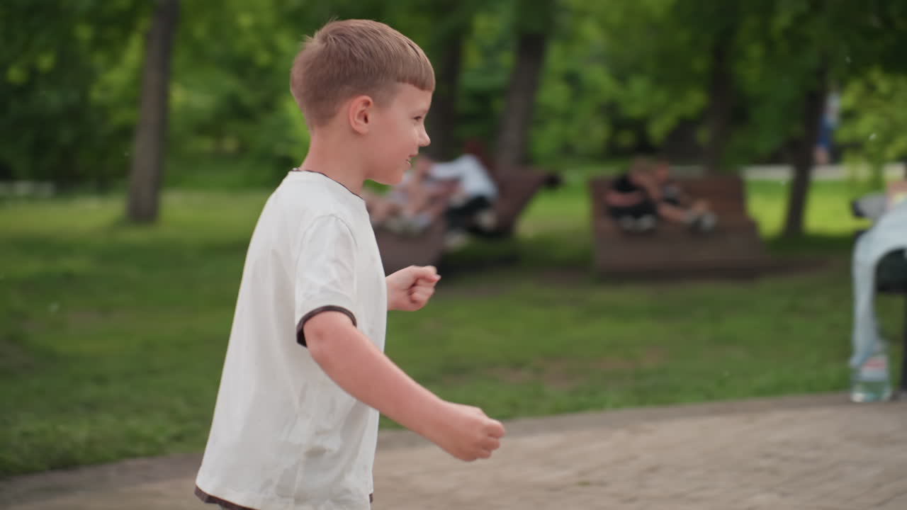 back view of boy running playfully followed by girl, children near benches around amusement park green trees background, joyful movement and summer leisure, summer park atmosphere and joyful motion