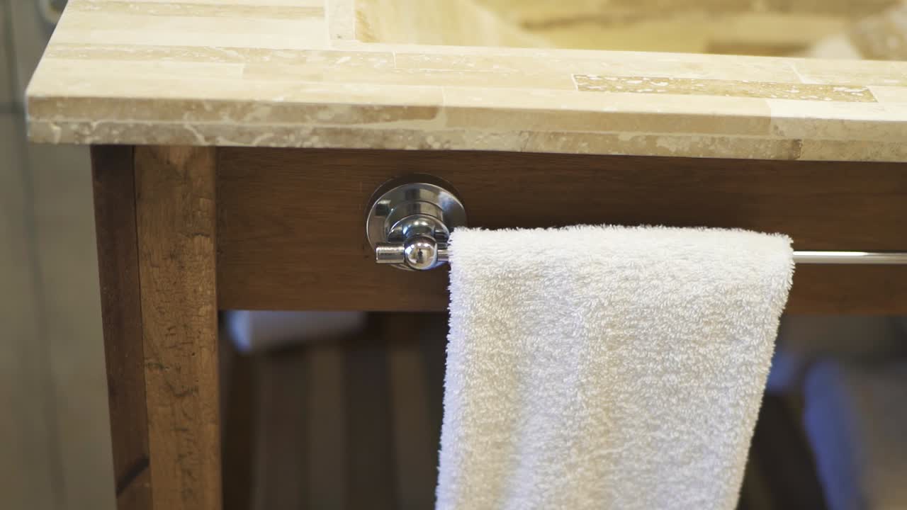 A slow-moving shot showcases bathroom furniture made of wood and nature stone, featuring a towel already hanging for guest use, emphasizing the luxurious and inviting atmosphere
