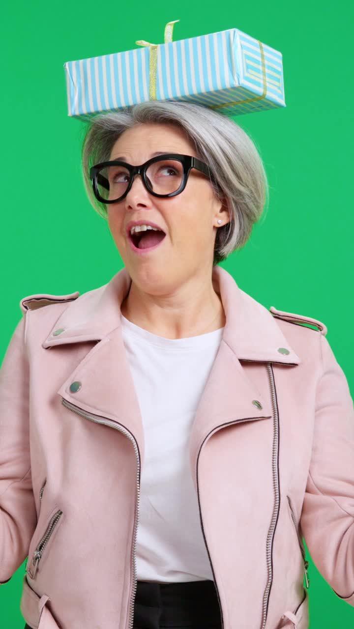 Donna giocosa che bilancia una scatola regalo sulla testa.
