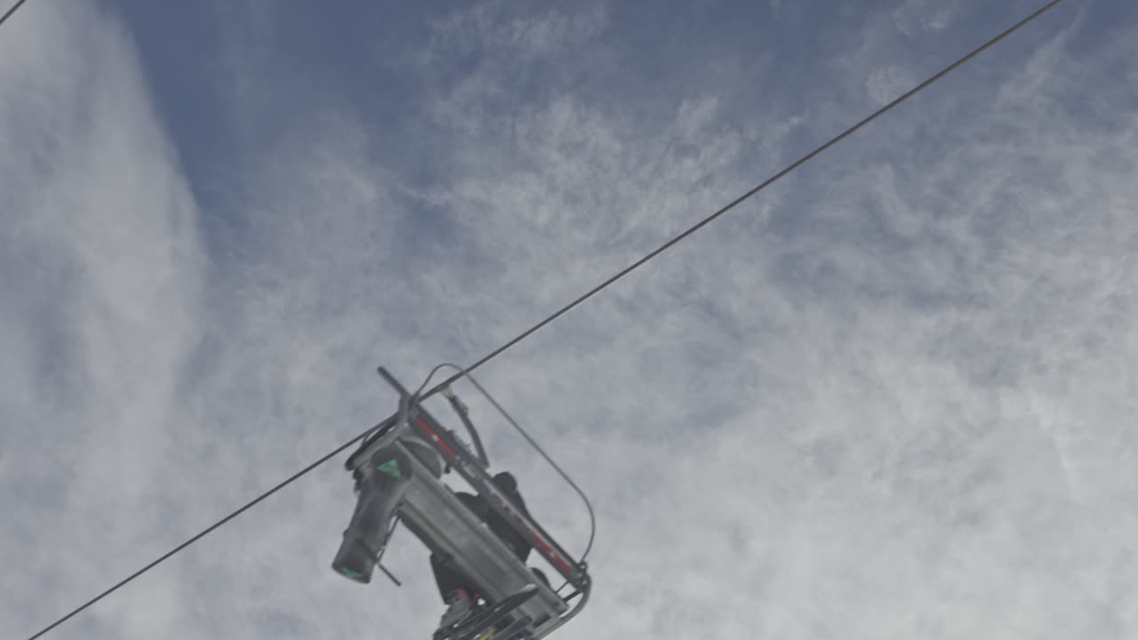 Skiliftstol med ski og snowboard bevæger sig hen over blå himmel.