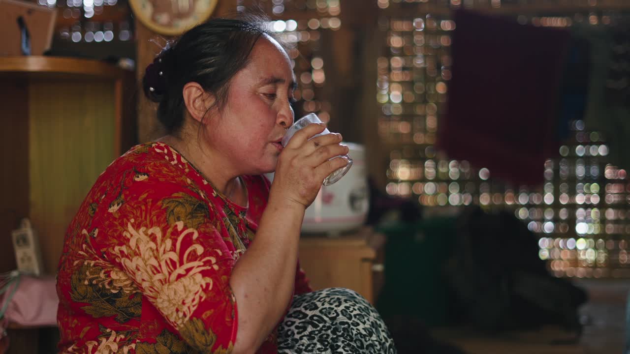 An Asian woman drinks from a glass indoors