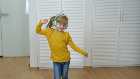 Niña-Pequeña-Con-Auriculares-Escuchando-Música-Y-Bailando-Curiosamente-Cerca-Del-Armario-En-Casa