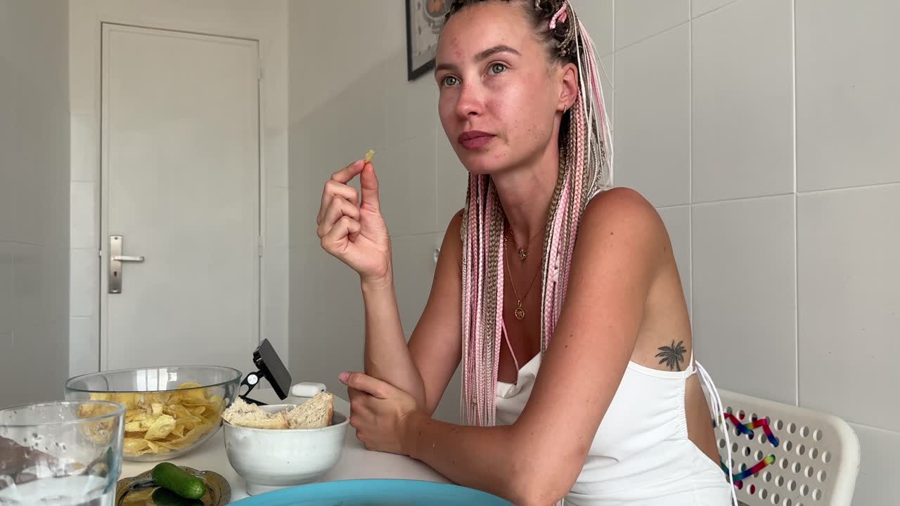 Mujer joven con trenzas comiendo papas fritas en una mesa de cocina