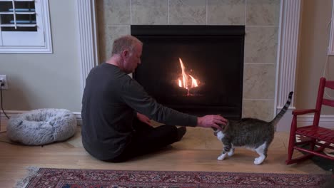 un hombre mayor se sienta con su gato mascota junto a la chimenea