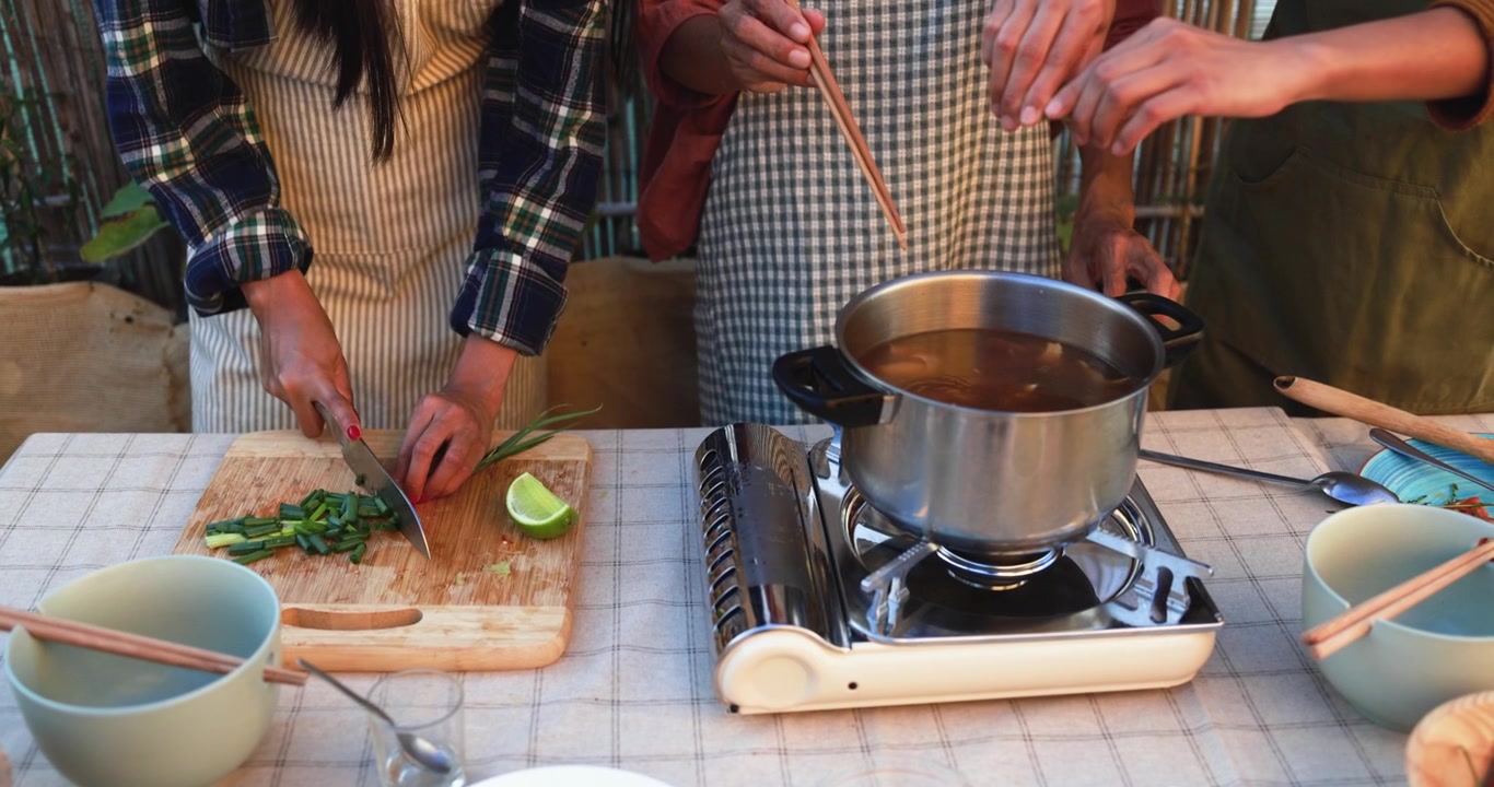 Primer plano de personas cocinando al aire libre, picando cebolletas y revolviendo sopa