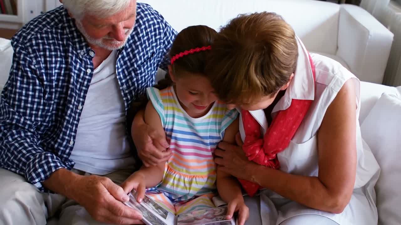 Nonni e nipote che esaminano l'album di foto in salone