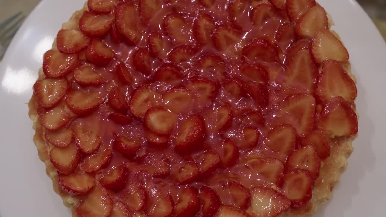 Top view of a strawberry tart covered with sliced fruit and shiny glaze on a dessert plate