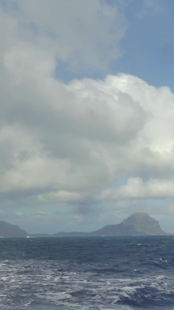 Arcobaleno su isola montuosa lontana e onde agitate dell'oceano