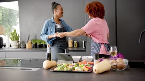 happy diverse couple in aprons having fun cooking and dancing together in kitchen, in slow motion