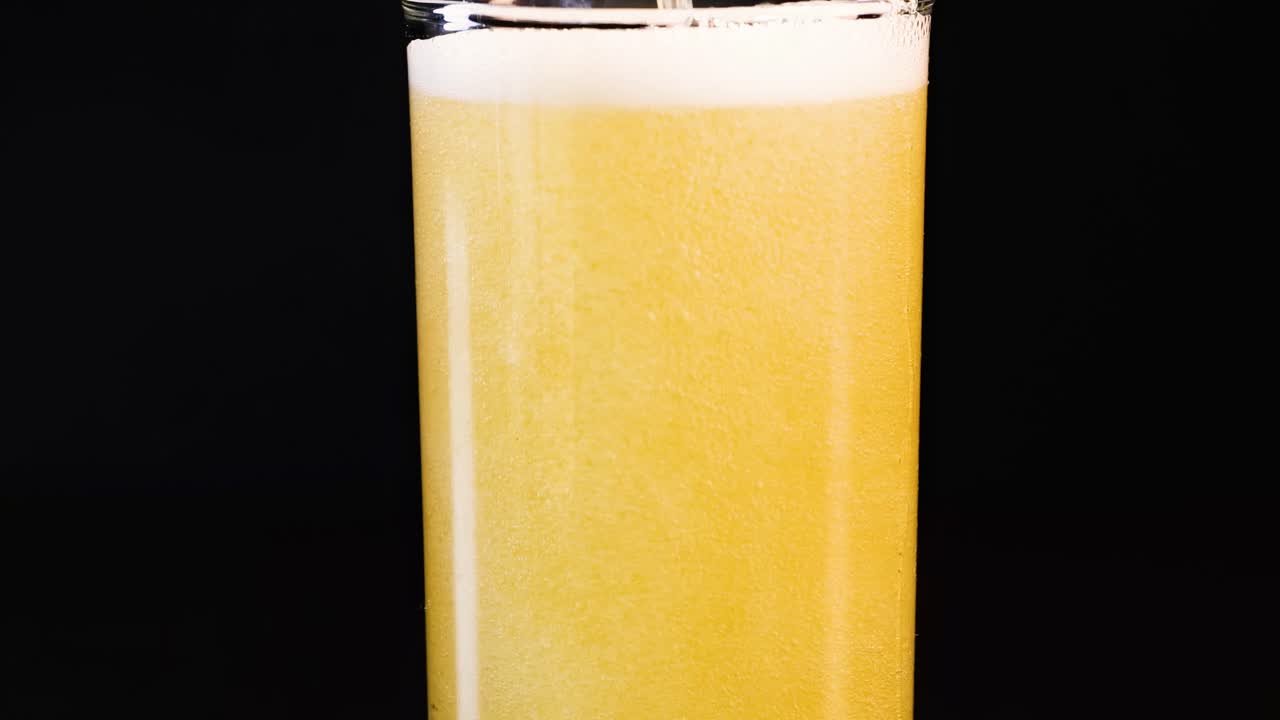 A golden drink is poured into a glass, showcasing the formation of foam and bubbles.