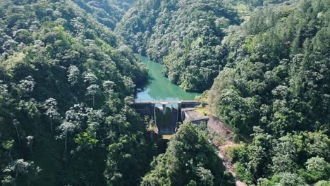 aerial backwards shot of tireo dam in deep jungle during sunny day on dominican republic island - panorama view