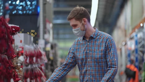 un hombre con una máscara protectora en una joyería y guirnaldas con juguetes para árboles de navidad y en casa. guirnaldas navideñas y decoración