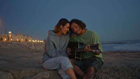 couple playing guitar on the beach at sunset