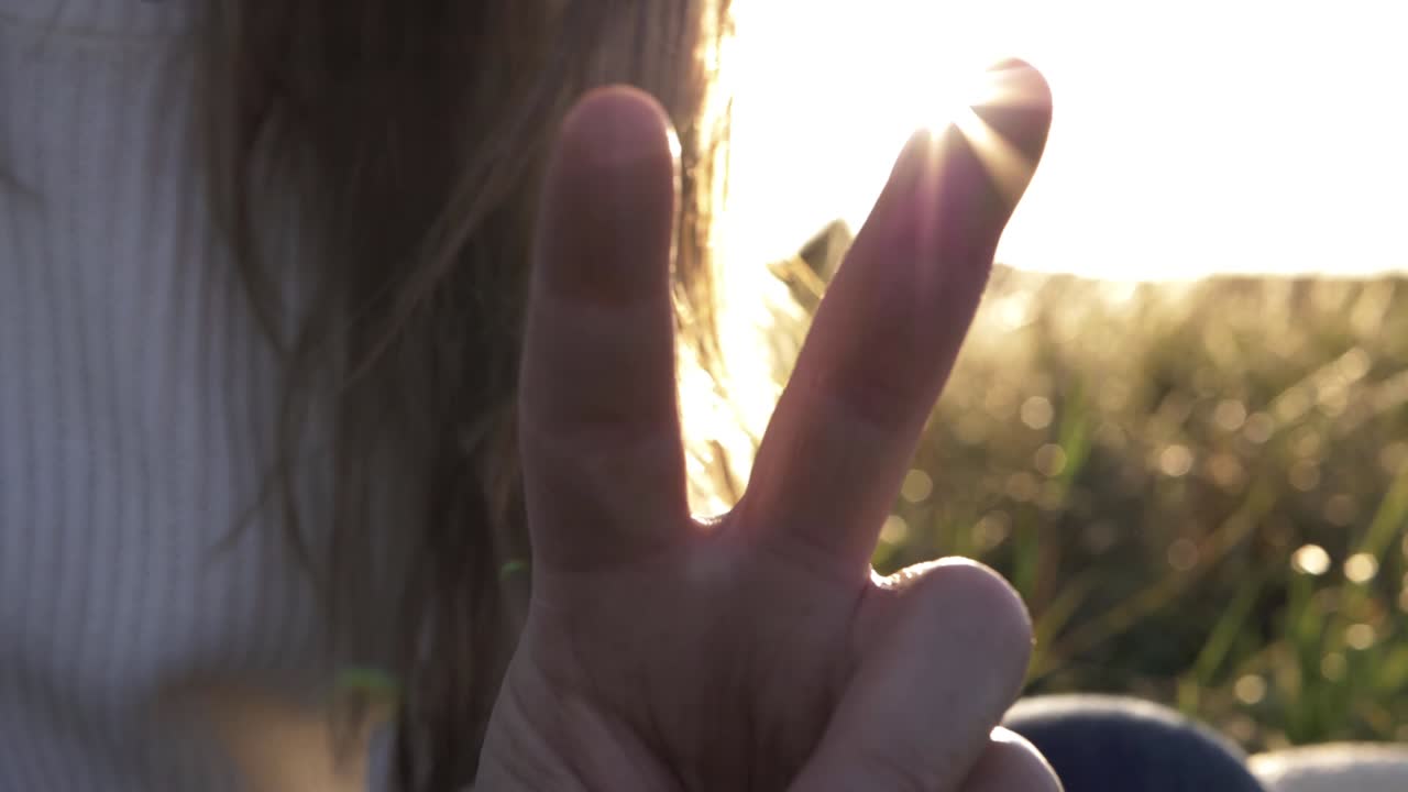 Woman holding up fingers in peace sign against sunshine background