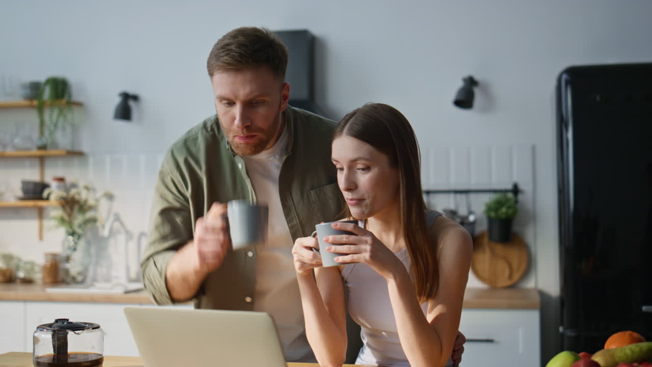 Smiling spouses looking laptop in kitchen enjoying morning together closeup