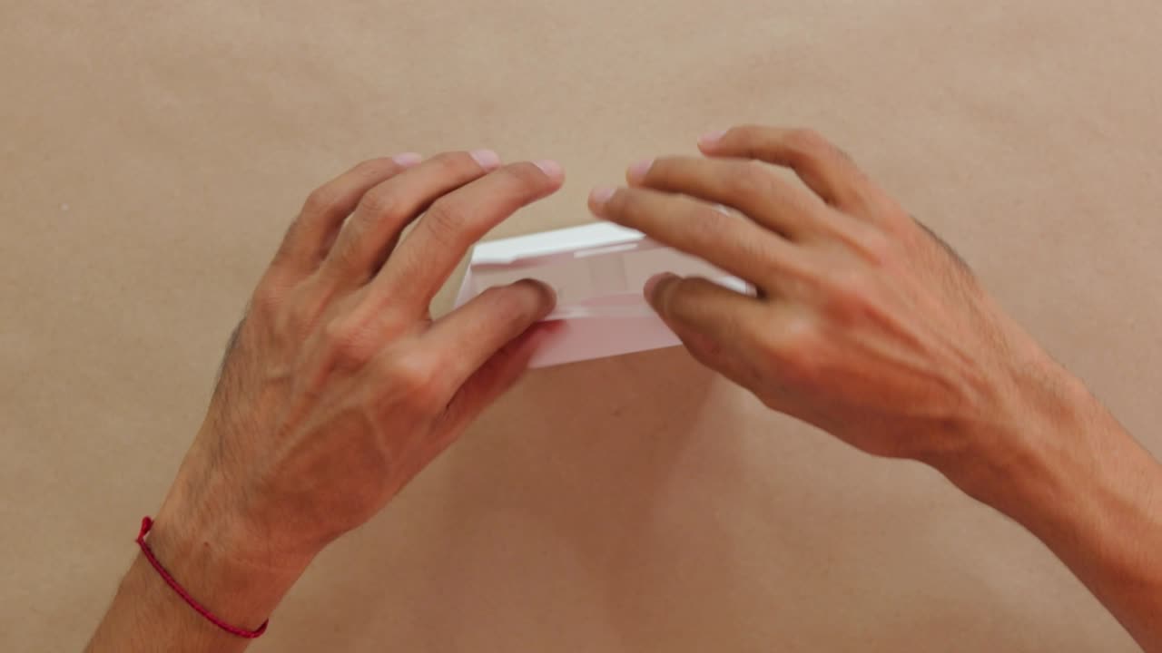 manos montando una caja de dulces blanca en una superficie beige, primer plano