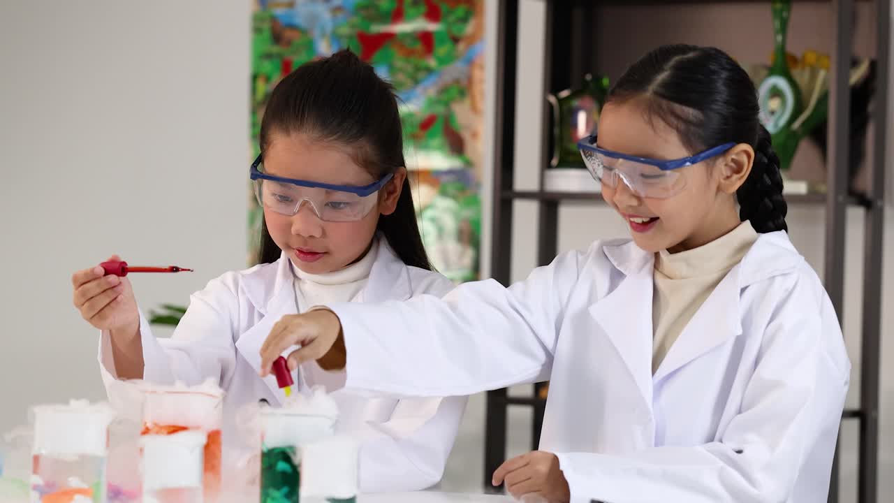 Dua gadis muda mengenakan jas lab menggunakan pipet untuk menambahkan cairan ke es kering yang berasap.