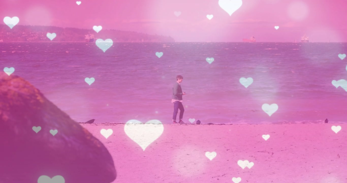 Stepping from rock, man strolling pink beach checking smartphone messages under floating hearts