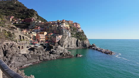 colorful buildings in manarola with rocky coastline and clear blue ocean on a sunny day