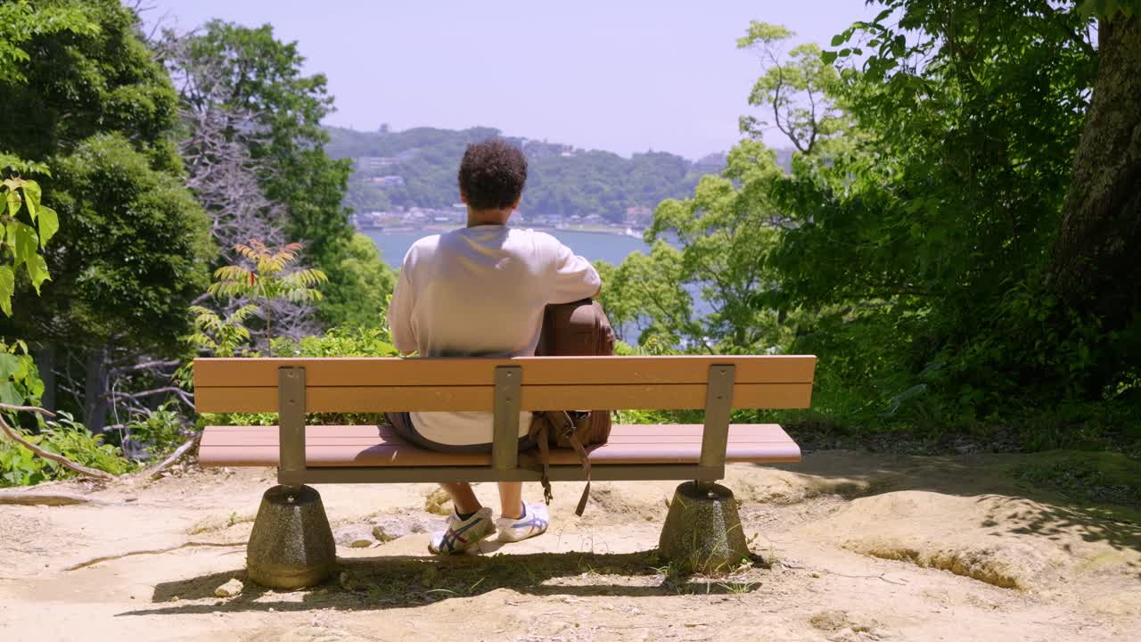 Young male traveler taking break on bench overlooking panoramic ocean