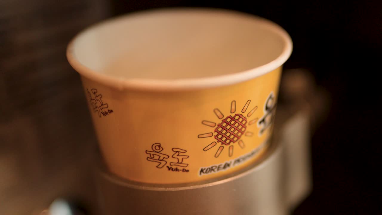 Close-up shot of an automated machine dispensing smooth vanilla soft serve into a paper cup