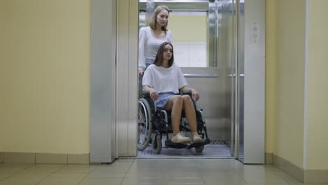 mujer rubia empuja a su hermana en silla de ruedas después de que se abre la puerta