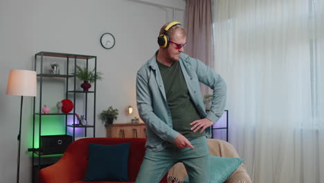 overjoyed young man in wireless headphones dancing, singing on cozy couch in living room at home