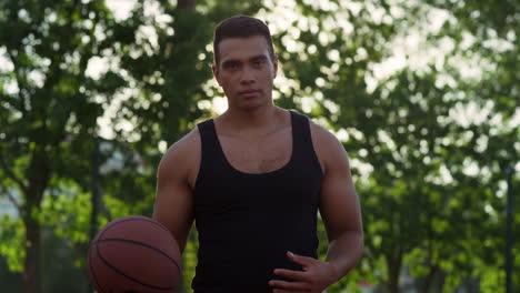 Focused-mixed-race-sportsman-practicing-basketball-in-playground-alone.