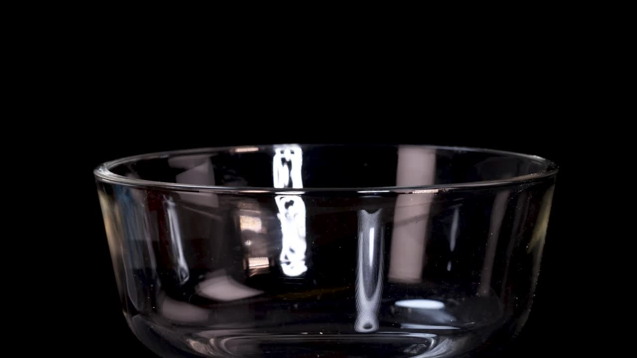 A block of uncooked instant noodles falls into a clear glass bowl against a black backdrop, captured in sharp, well-lit slow motion with a static camera