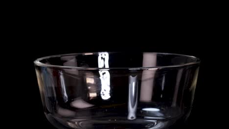 a block of uncooked instant noodles falls into a clear glass bowl against a black backdrop, captured in sharp, well-lit slow motion with a static camera