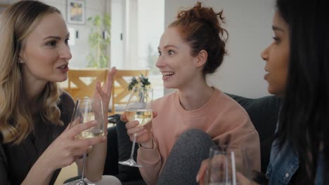 tres amigas caucásicas y de raza mixta sentadas en el sofá, charlando y bebiendo vino.