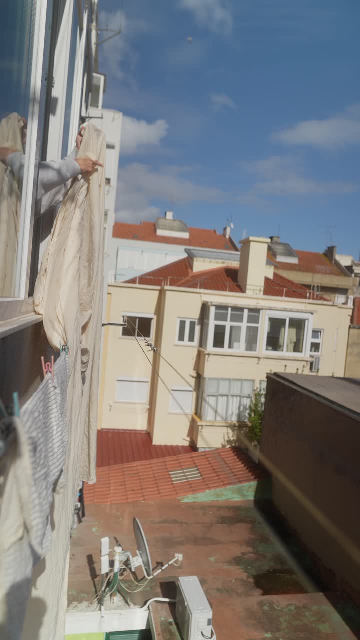 Woman hanging clothes on a clothesline from a window.