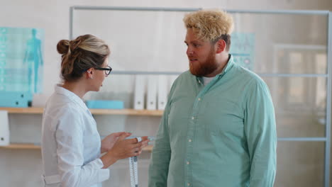 female doctor measuring waist of obese man in clinic