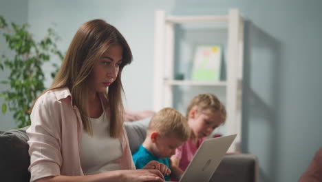 Lady-types-on-laptop-quiet-children-watch-video-via-tablet