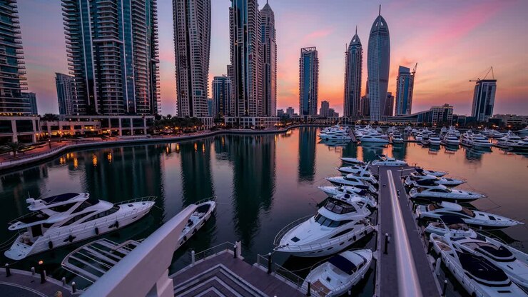 Orange and purple sunrise illuminating Dubai Marina with luxury yachts moored at the piers and modern skyscrapers reflecting on the calm water