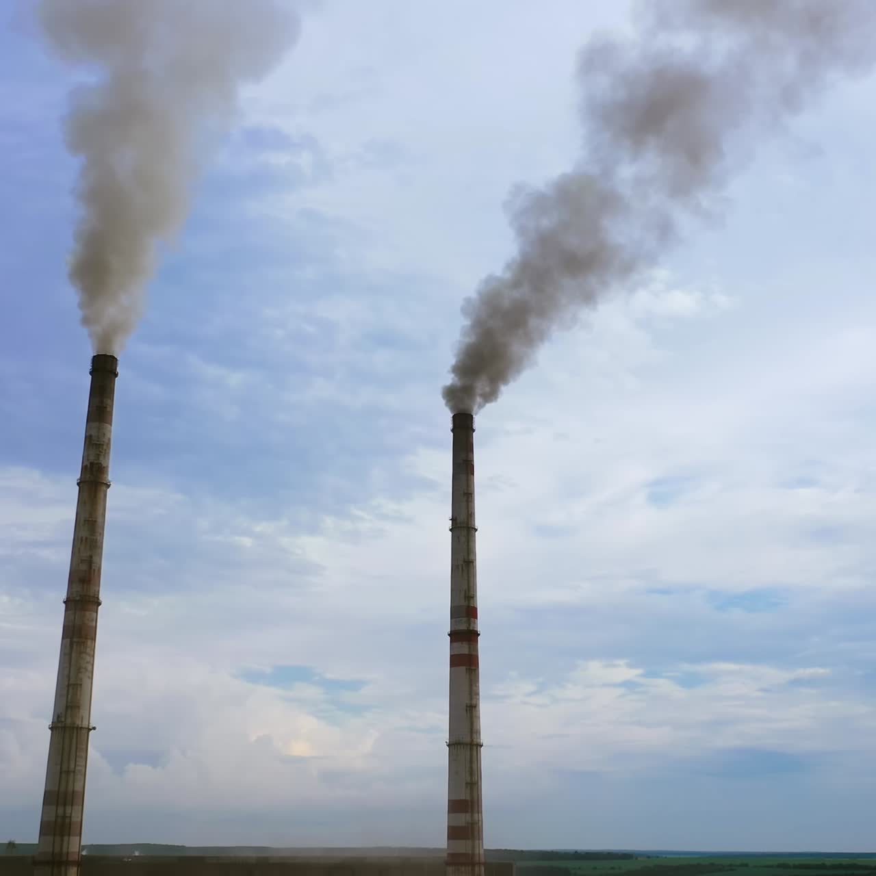 Enterprise chimneys tubing against the sky background release black smoke. Dangerous smoke against blue sky. Factory pollutes the environment