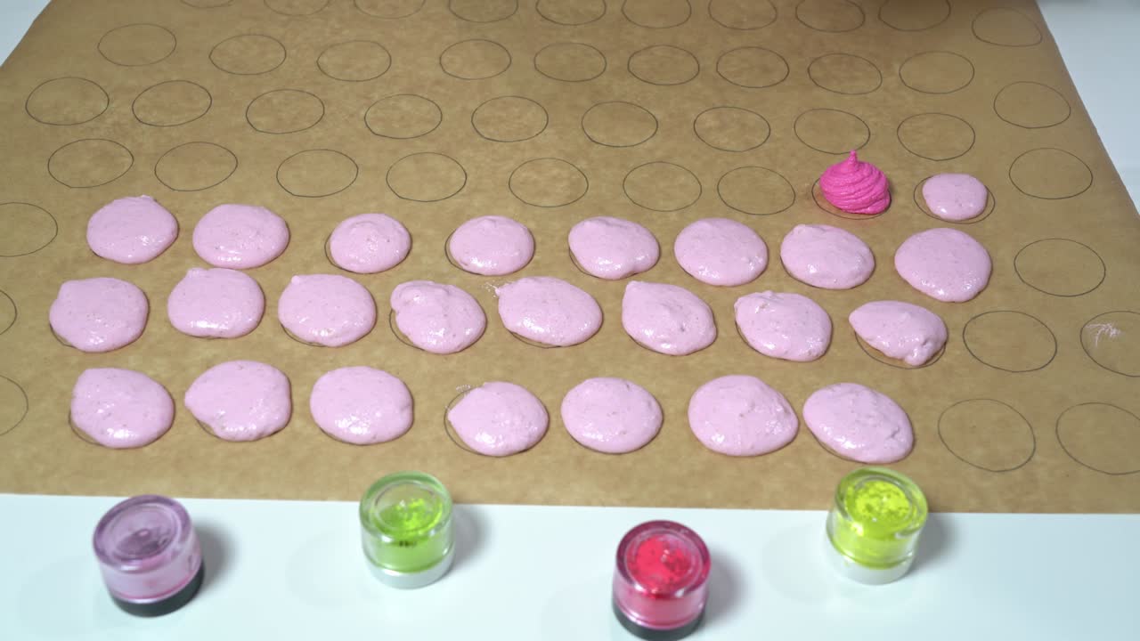 panadero usando una bolsa de pastelería para llenar formas circulares en papel de pergamino con un tono de color diferente de masa rosa. fabricación de macarrones.