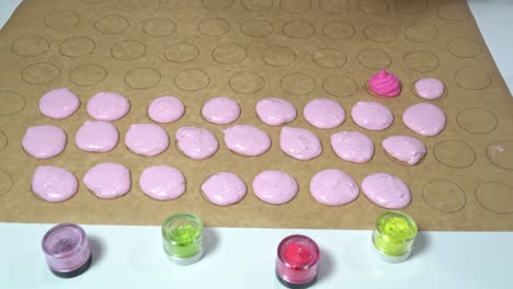 baker using a pastry bag to fill out circular shapes on parchment paper with a different colored shade of pink batter. making of macarons.