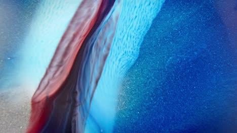 Vivid contrast of red and blue inks merging in water, with a sparkling effect resembling a cosmic nebula