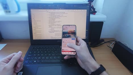 persona que trabaja en una computadora portátil pero posterga el desplazamiento por las redes sociales en un teléfono inteligente