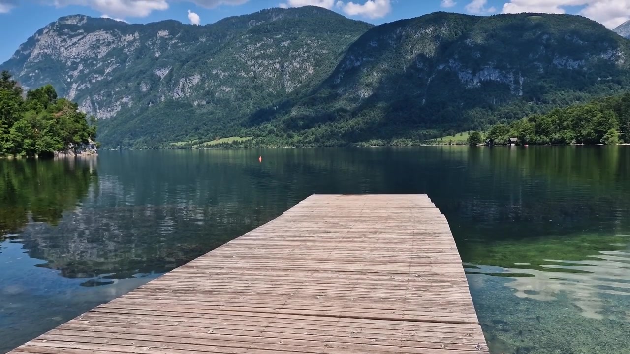 Træbro ved sø i malerisk alpelandskab, med spejlinger i vandet. Bohinj-søen, Slovenien.