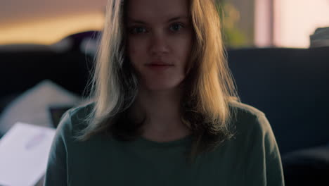 cinematic close up of a young white woman smiling and waving straight into the camera during a golden hour sunrise in her apartment in the morning in slow motion