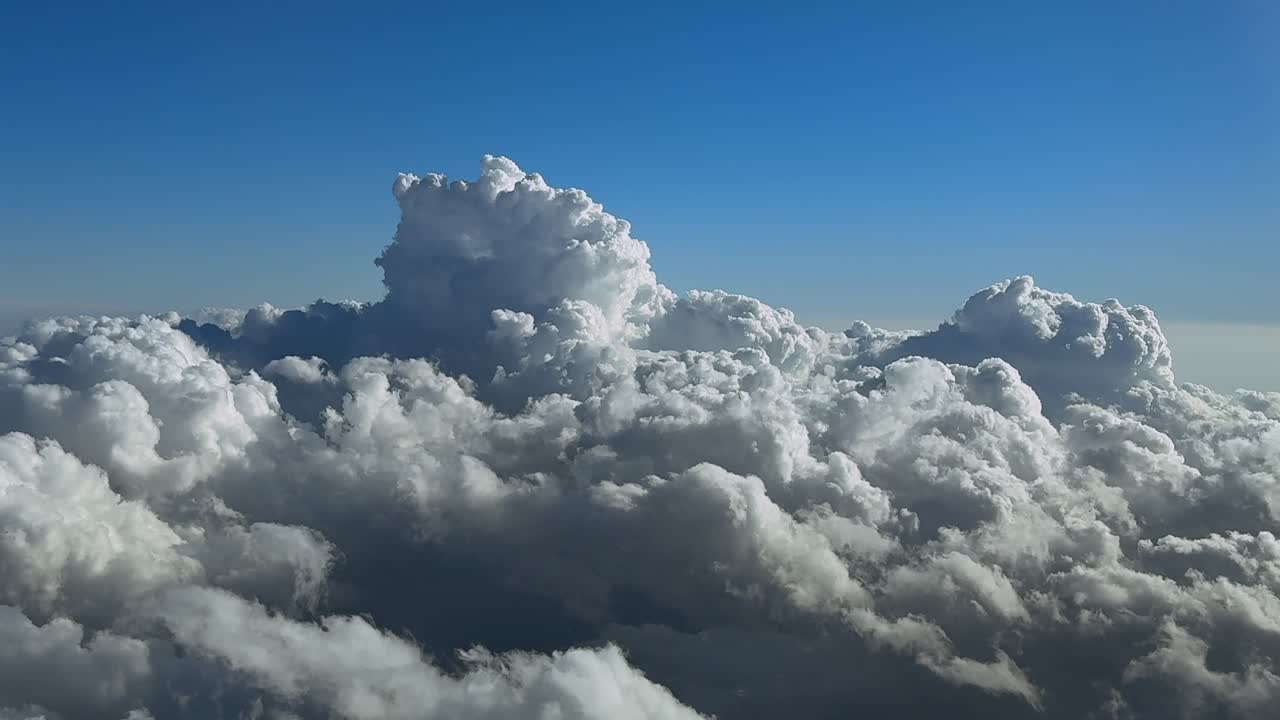 An immersive pilot’s eye view taken from the cockpit of a jet airplane flying over a layer of cottony clouds, with a elvolving storm cloud ahead, illuminated by the sunset light
