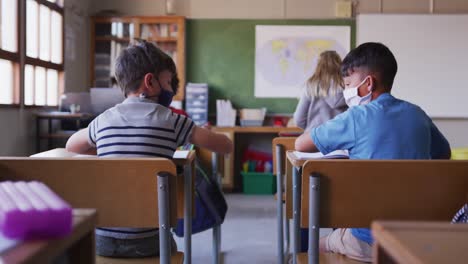 Zwei-Jungen-Mit-Gesichtsmasken-Begrüßen-Sich-In-Der-Schule,-Indem-Sie-Ihre-Ellbogen-Berühren