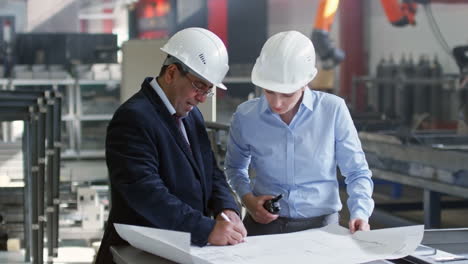Ingenieure-In-Eleganter-Kleidung-Und-Helmen-Beraten-Sich-Beim-Treffen-über-Details-Der-Skizze-Auf-Dem-Plan