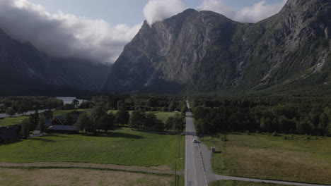 Vista-Aérea-De-Un-Automóvil-Conduciendo-Por-Una-Carretera-En-Medio-De-Un-Valle-Verde-Y-Tierras-De-Cultivo-En-Romsdalen,-Noruega---Disparo-De-Un-Dron